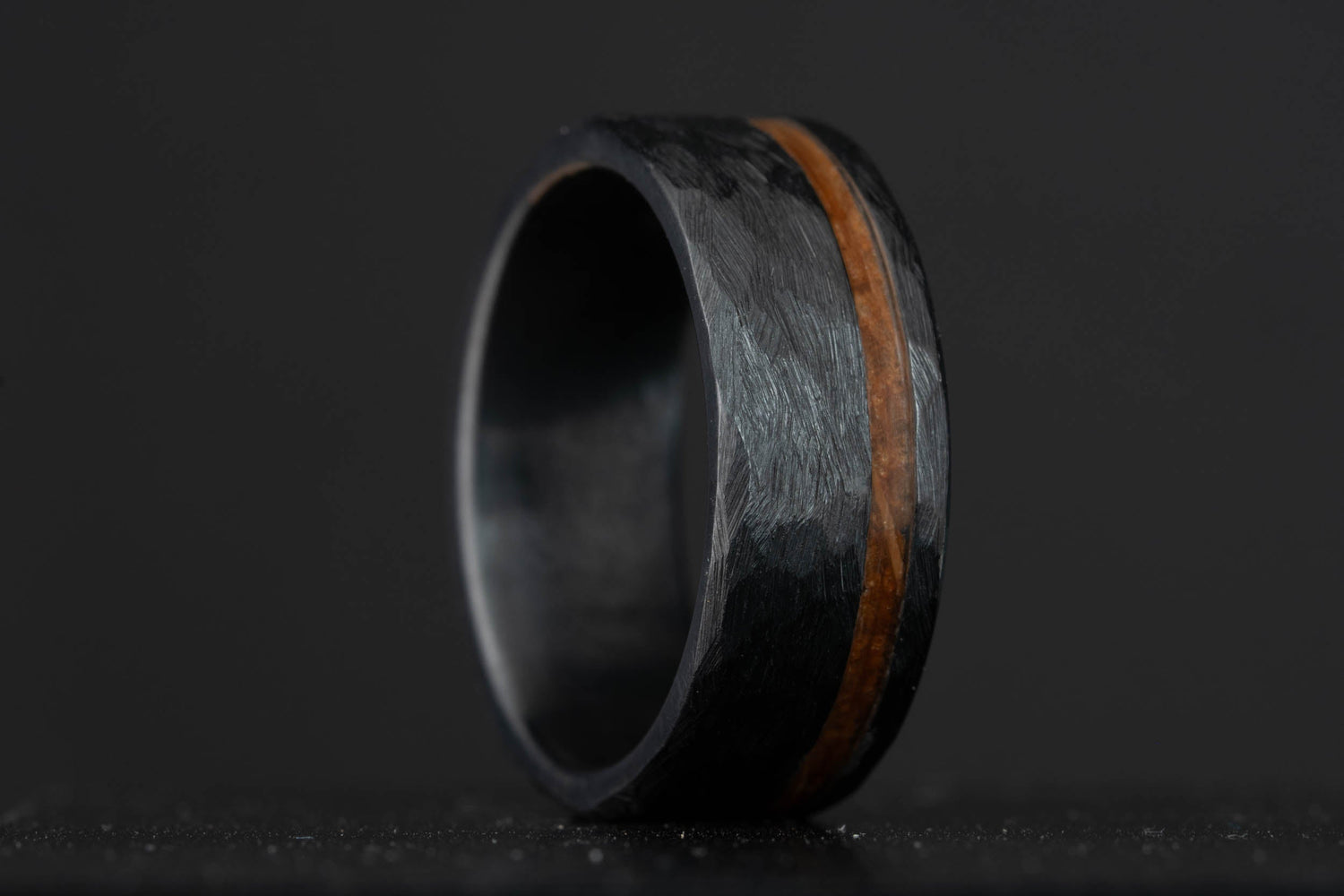 Black hammered titanium wedding band with a bourbon barrel stave oak inlay, crafted from charred white oak.