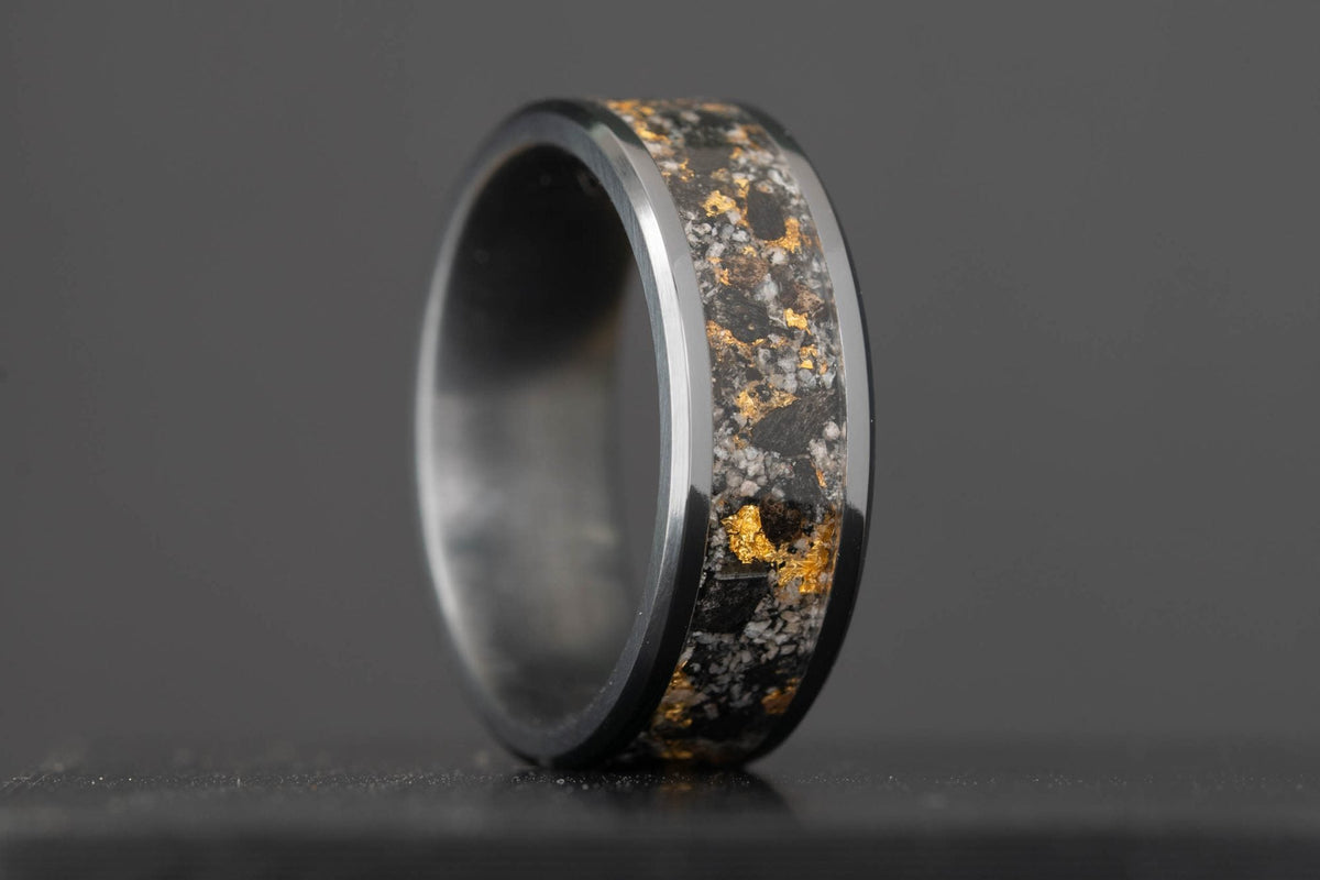 Black titanium wedding band with an inlay of crushed megalodon tooth, 24k gold leaf, and Yooper Glow Stone, shown in normal light.