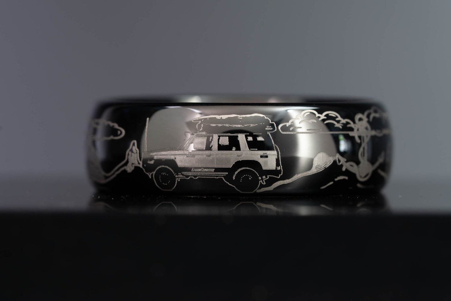 Custom engraved black tungsten wedding band featuring a Land Cruiser, Glass House Mountains, clouds, anchor, and waves
