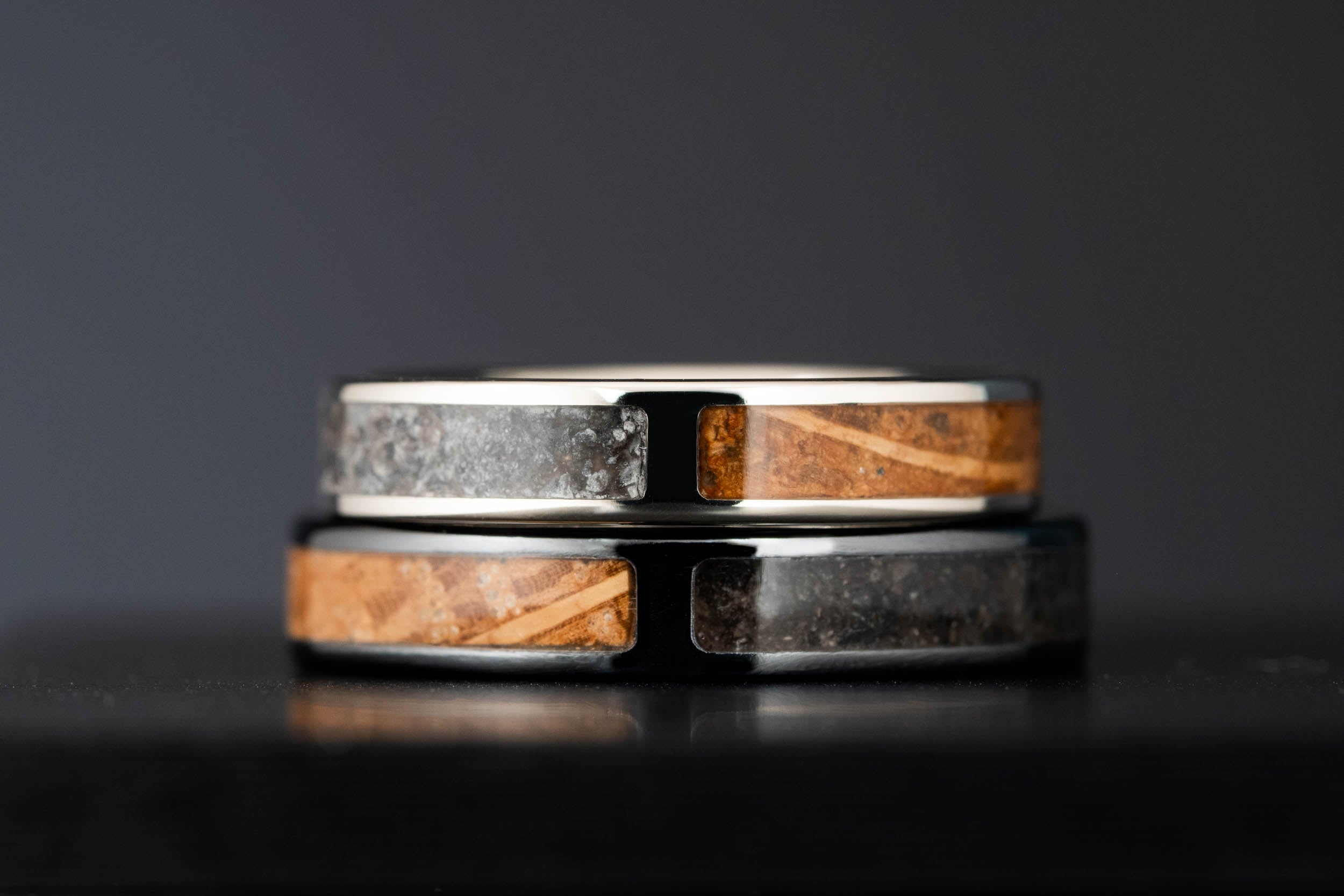 Stacked view of handmade wedding rings with split inlay design, combining crushed stone and wine barrel oak in gold and titanium bands.