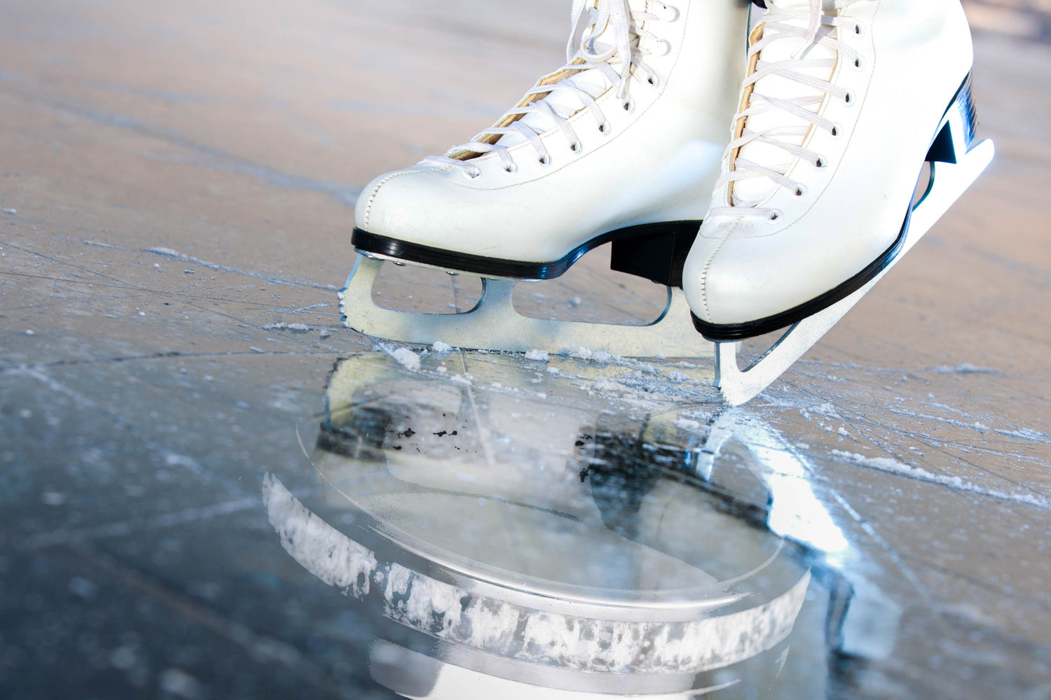 White figure skates gliding on ice, symbolizing the inspiration behind a custom wedding ring made with an ice skate blade inlay by Honest Hands Ring Co.