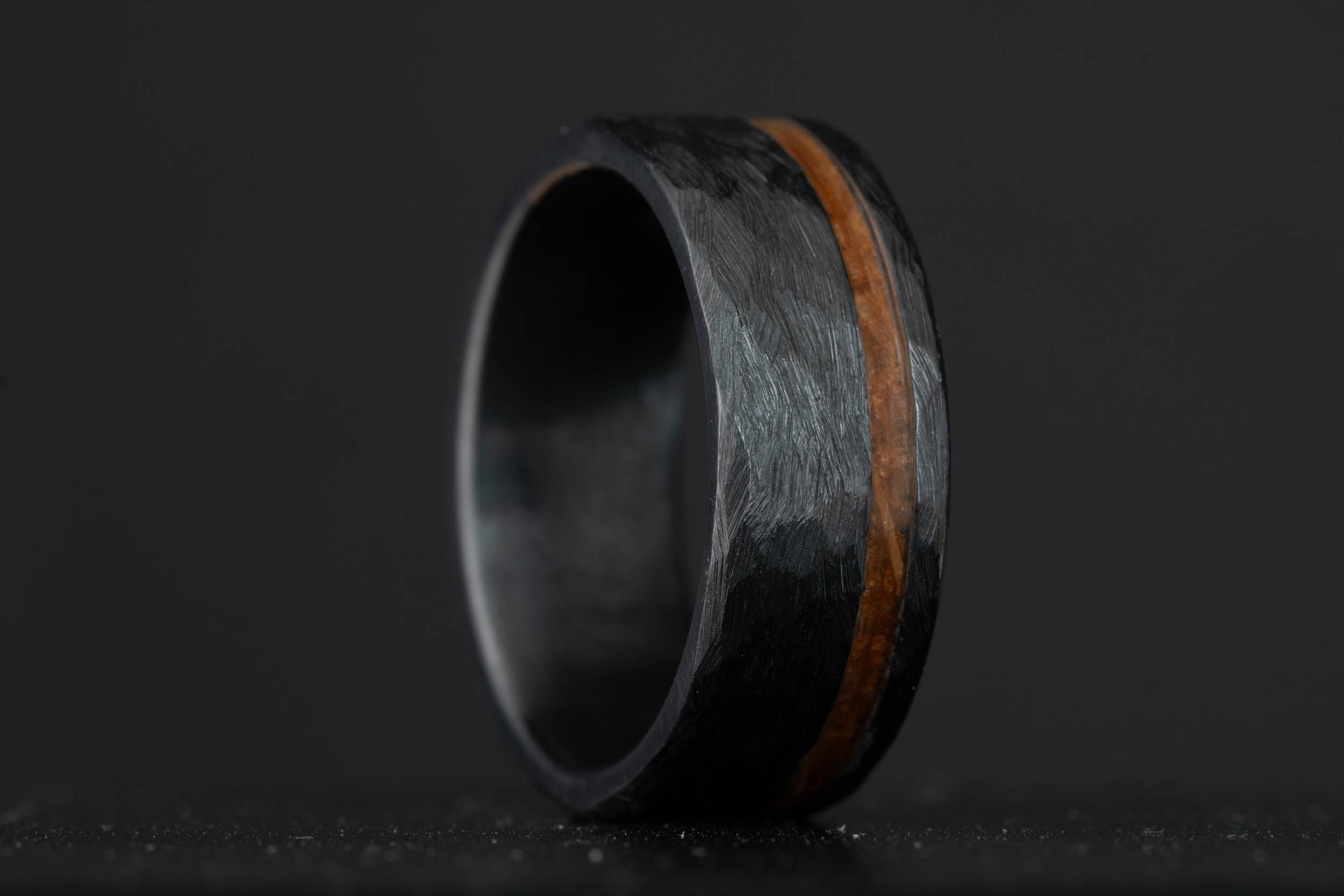 Black hammered titanium wedding band with a bourbon barrel stave oak inlay, crafted from charred white oak.