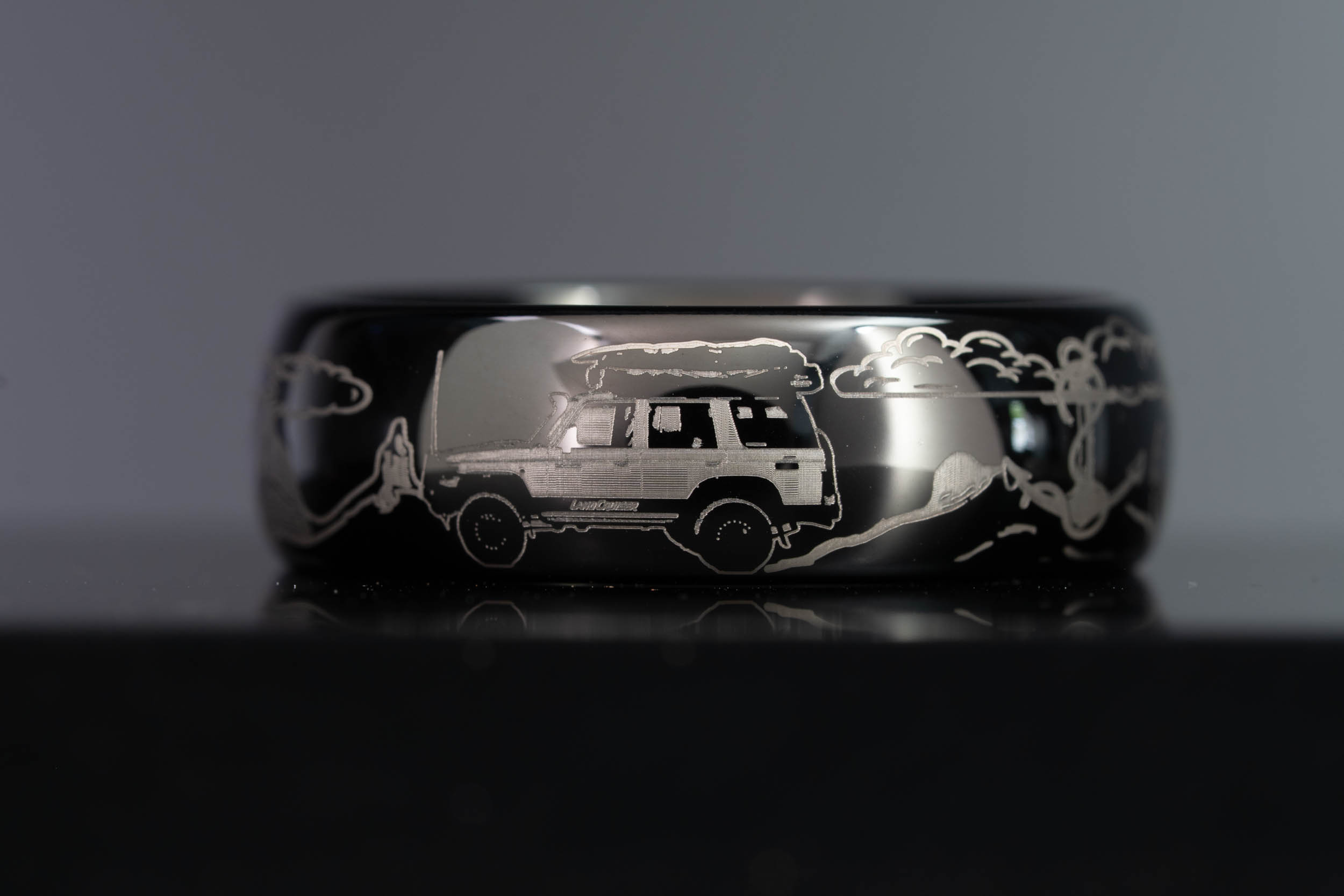 Custom engraved black tungsten wedding band featuring a Land Cruiser, Glass House Mountains, clouds, anchor, and waves