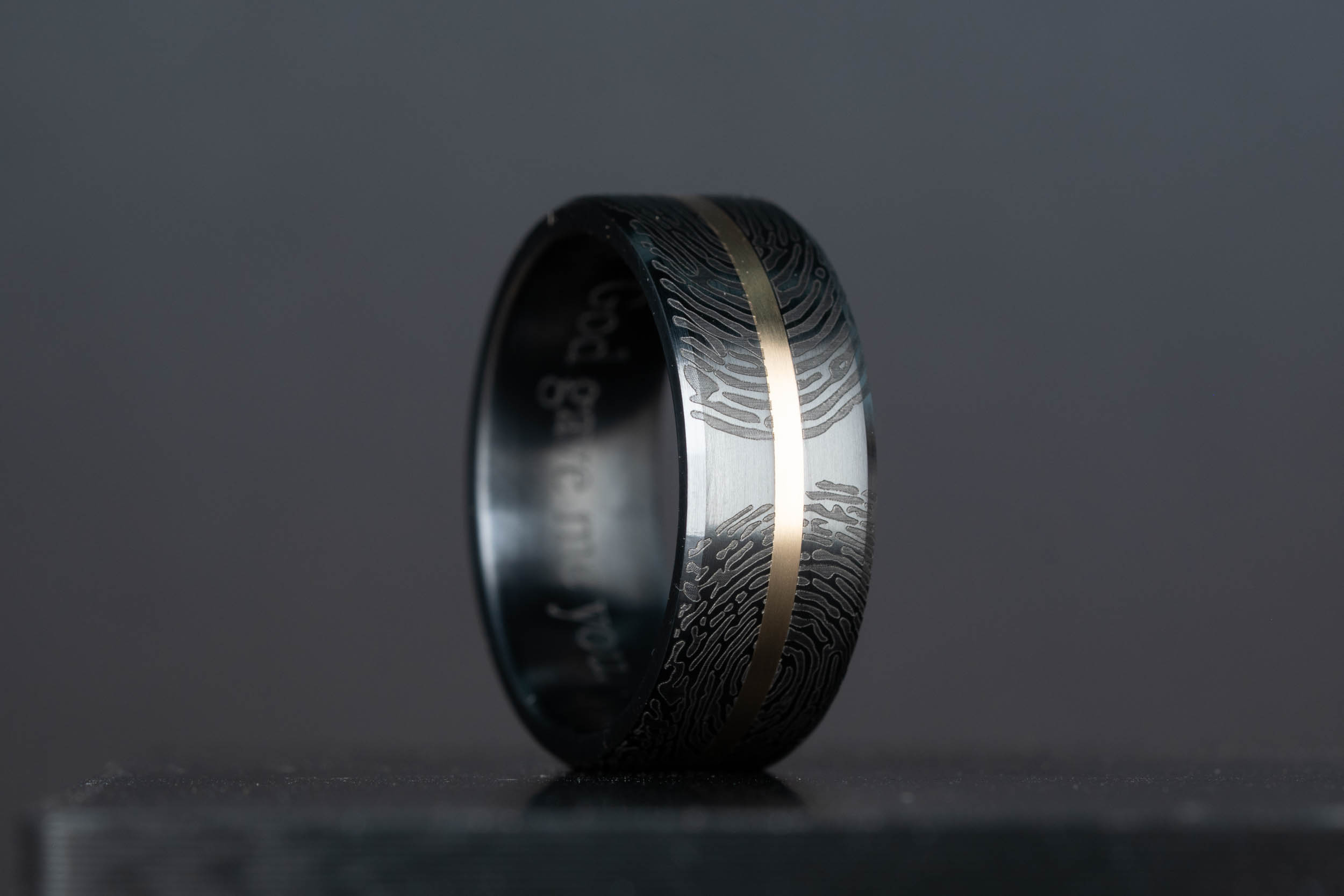 Custom black titanium wedding band with 14k yellow gold center inlay and dual fingerprint engraving, handcrafted by Honest Hands Ring Co.