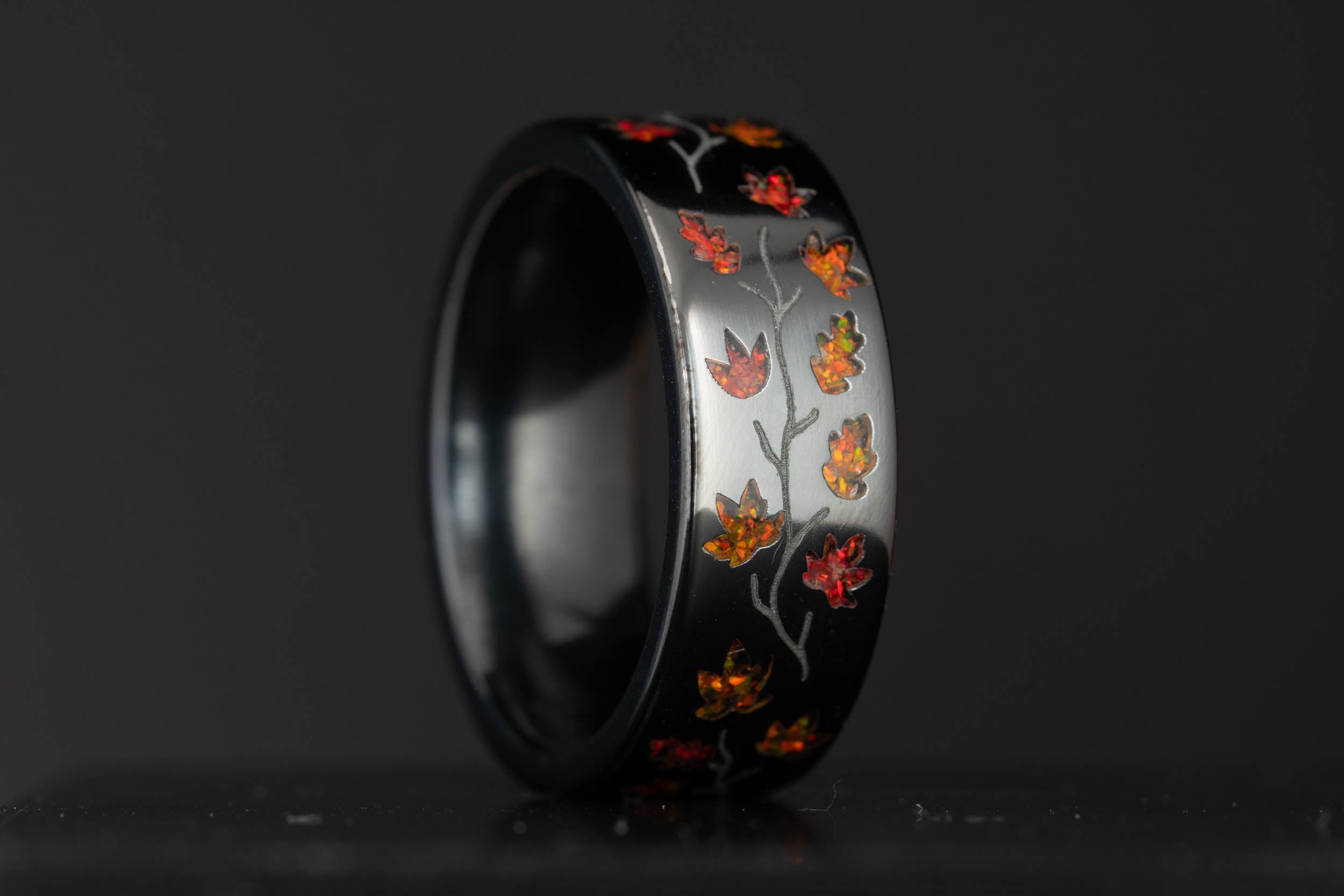 Honest Hands black titanium ring with engraved cross and script names, fire opal autumn leaves wrapping the band.