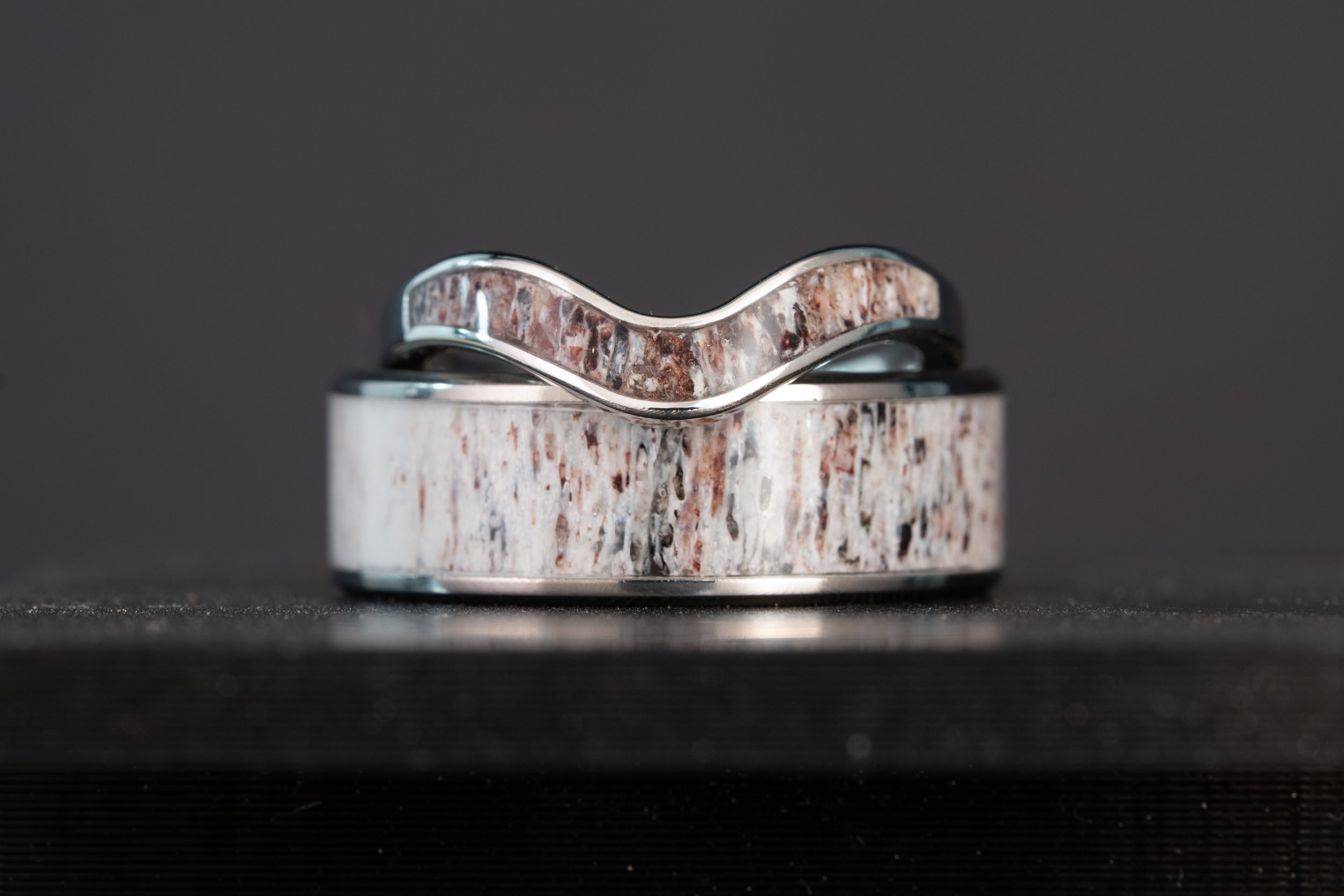 Wide studio shot of the stacked elk antler wedding bands, showing the cream, rust, and black grain pattern in the antler inlay.