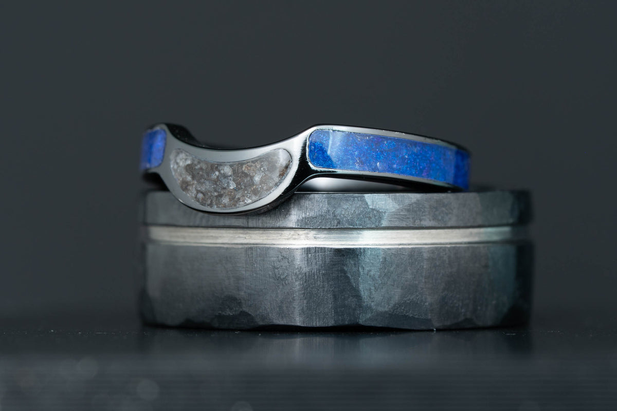 Finished Honest Hands wave-cut ring with alexandrite and lunar meteorite inlay, resting on the hammered black titanium band, studio lit against a dark background.