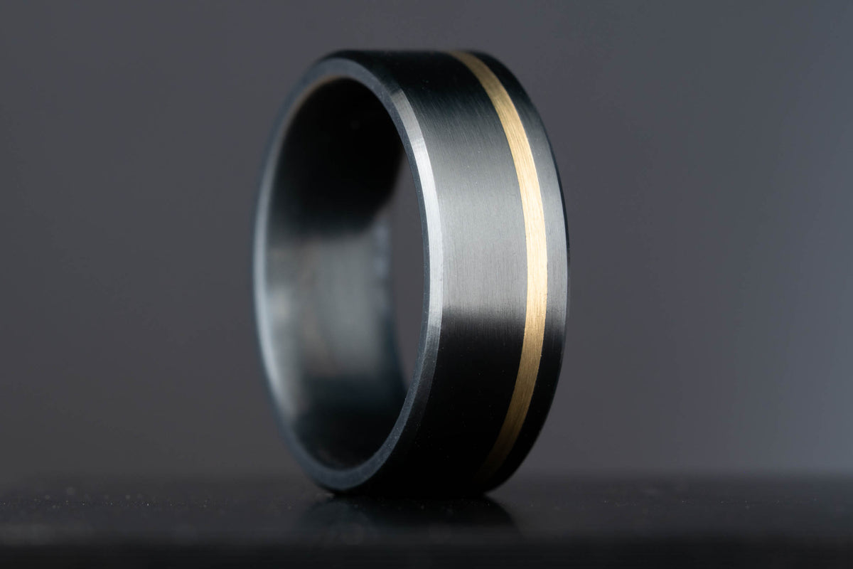 Finished Honest Hands wedding band in black titanium with a single brass inlay line, handcrafted in Colorado.